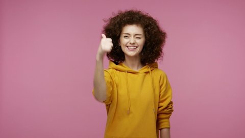 Clever young woman afro hairstyle in hoodie thinking pointing finger up and having great idea, showing thumbs up, surprised by suddenly found smart solution. indoor  isolated on pink background