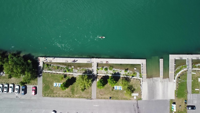 Aerial top down shot of parking cars beside river with person paddling on sup board during sunny day in Canada.