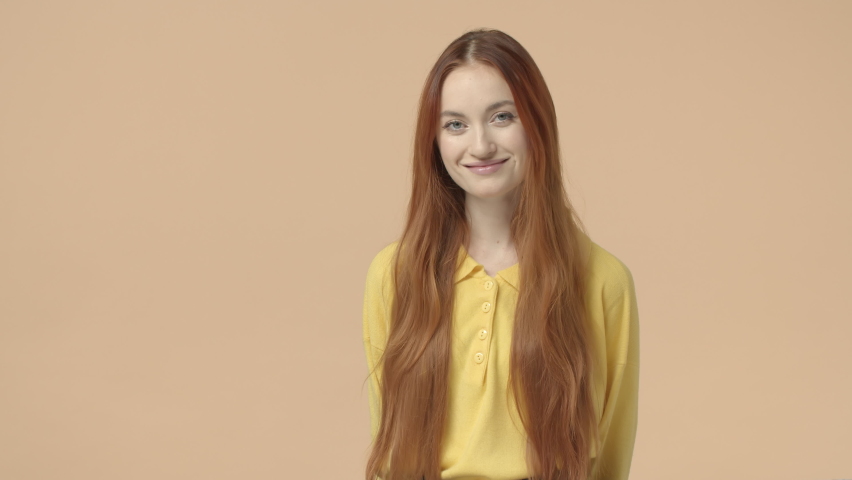 Youth, emotions and beauty concept. Shy attractive woman with long red hair, natural ginger, smiling happy and coy, hold hands behind head, express joy, enthusiasm, being modest, yellow background