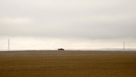 Pickup truck driving left to right on rural road in arid farm landscape during winter, static long shot