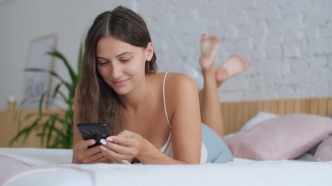 Leisure at home, Stay in the house, Beautiful woman, home weekend. Woman lying on bed in bedroom and chatting using smartphone