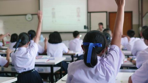 Slow motion of Asian high school students in white uniform actively study science by raising their hands to answer questions on projector screen that teachers ask them  in science classroom.