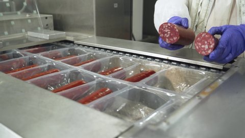 Meat production, woman worker in protective uniforms pack and stack raw smoked sausages, the process of packaging ready-made smoked sausages in plastic packaging, food industry.