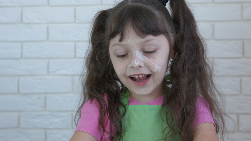 Enjoying the dough. A smiling little girl enjoy to cook and strew the flour on the dough in the kitchen.