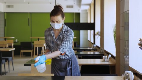 waitress, wearing protective gloves and mask, disinfects tables for visitors using antiseptic spray for protect coronavirus. reopening cafeteria or restaurant. safety concept.