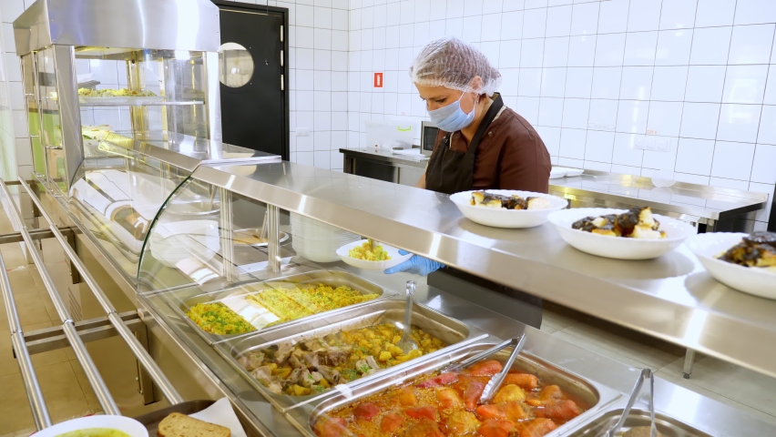 Waitress, in protective gloves and mask, puts food on plates and serves to customers in self-service cafeteria or buffet restaurant. reopening after covid-19. safety concept. health food. | Shutterstock HD Video #1058466187