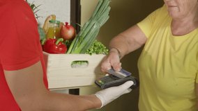 SLOW MOTION, CLOSE UP: Elderly woman uses a credit card to pay for her grocery delivery during the coronavirus pandemic. Senior lady pays for fruit and vegetable delivery during coronavirus pandemic - Powered by Shutterstock - Get 15% off with code: PIKWIZARD15