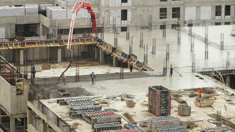 Workers at construction site pour and level concrete. Modern monolithic industrial construction. Large construction site of residential building.