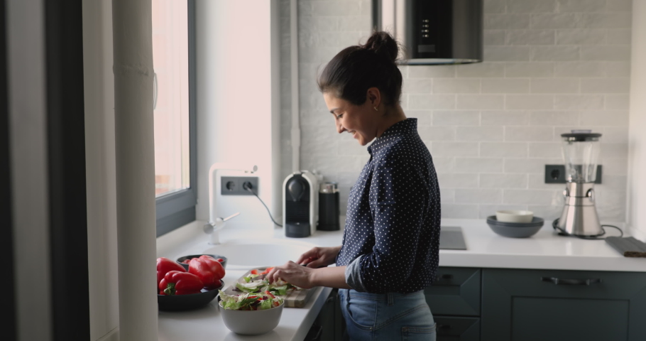 30s indian woman standing in domestic modern home kitchen preparing healthy vegetable salad smiles enjoy process. Satisfied housewife client of easy convenient fast fresh organic food delivery concept | Shutterstock HD Video #1058470567