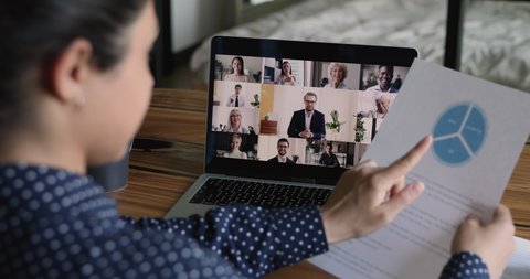 Team of multiethnic colleagues pc screen view over businesswoman executive shoulder hold paper with pie chart financial report forecast, makes presentation during group meeting by video conference app
