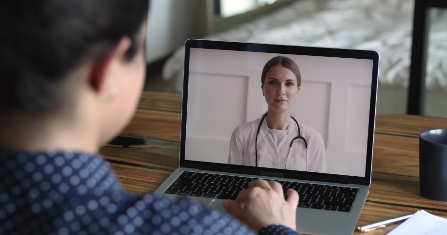 Therapist cardiologist provide medical heart disease consultation to client by video call, laptop screen view over patient shoulder sit at desk got help from woman practitioner doctor in white coat Royalty-Free Stock Footage #1058470684