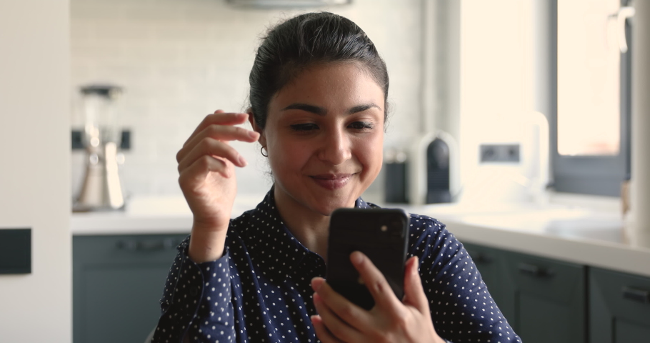 Indian ethnicity business woman freelancer sit at home studio apartments holding mobile phone modern wireless device. Woman looks at screen talking with colleague friend or client using video Royalty-Free Stock Footage #1058470690
