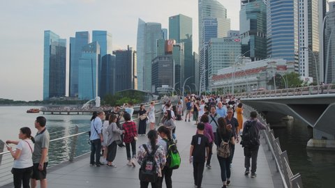 SINGAPORE - JANUARY 10, 2020: Crowd of tourists exploring city. People on bridge in Merlion Park with business towers in background. In 2019 tourism contributed about 4 per cent of Singapore GDP