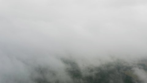 Aerial top view drone flies through heavenly beautiful fluffy rain clouds rolling over green forest. Foggy morning in pine woodland from above, cloudy, misty weather. Camera flight in low cloud in sky