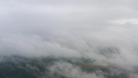Aerial top view drone flies through thick rain clouds rolling over green forest. Foggy morning in pine woodland from above, cloudy weather. Camera flight in low cloud in sky