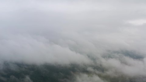 Aerial top view drone flies through heavenly fluffy rain clouds rolling over green forest and field. Foggy morning in pine woodland from above, cloudy, misty weather. Camera flight in low cloud in sky