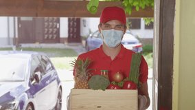 SLOW MOTION, CLOSE UP, PORTRAIT: Cheerful man delivers a box of fresh groceries at your doorstep. Young delivery man brings vibrant organic produce to your home during the coronavirus lockdown. - Powered by Shutterstock - Get 15% off with code: PIKWIZARD15