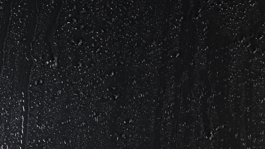 4K High quality footage of Rain on Window Sky Drops, White Drops of rain trickling down on black background. Rain Drops Falling down on black background.  Close up Slow Rain in slow motion.  Droplets 