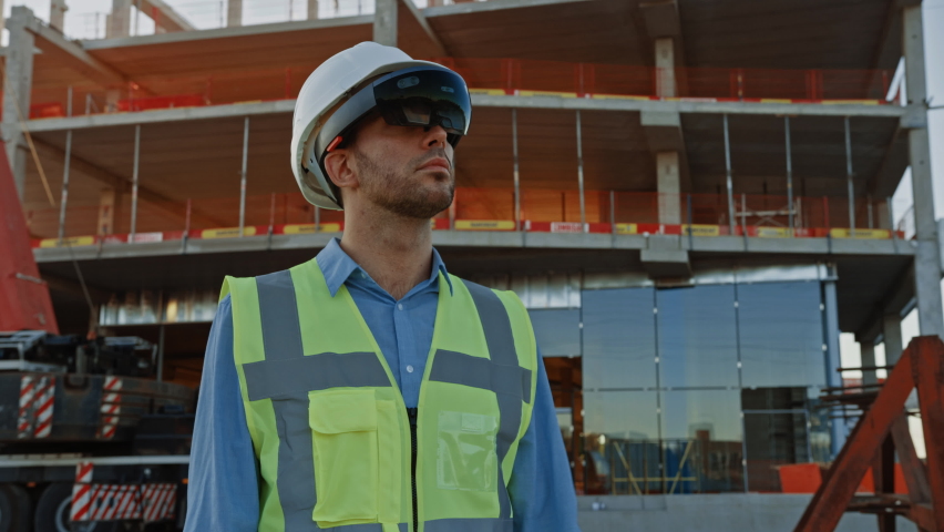 Futuristic Architectural Engineer Wearing Augmented Reality Headset, Uses Gestures to Create 3D Graphics VFX Model of a Building with Infographics. In Background Construction Site in Progress | Shutterstock HD Video #1058475670