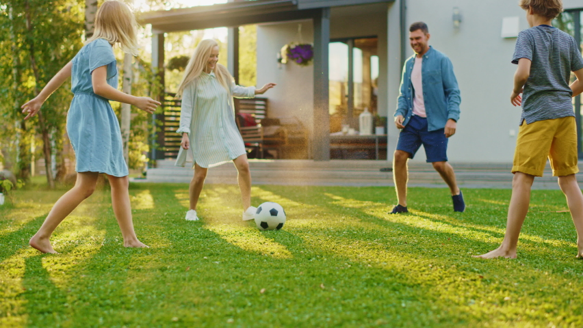 Happy Family of Four Playing Soccer, Passing Football to Each Other. Mother, Father, Daughter and Son Have Fun Playing Games in the Backyard Lawn of Idyllic Suburban House on Sunny Summer Day Royalty-Free Stock Footage #1058475676