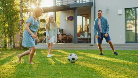Happy Family of Four Playing Soccer, Passing Football to Each Other. Mother, Father, Daughter and Son Have Fun Playing Games in the Backyard Lawn of Idyllic Suburban House on Sunny Summer Day