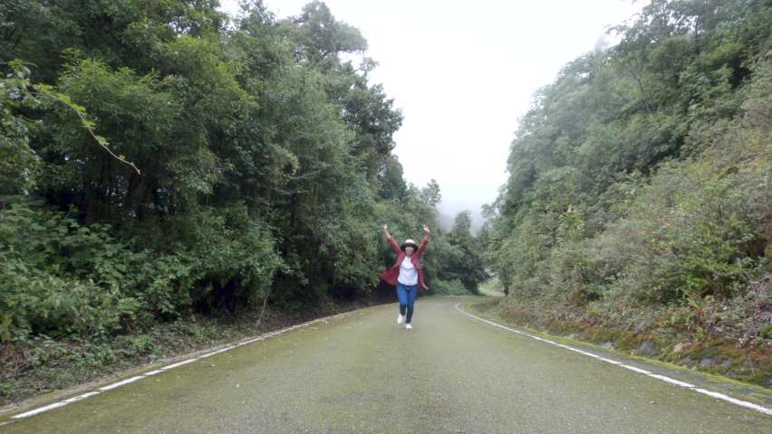 Female traveler running and relaxation on asphalt road among nature around.