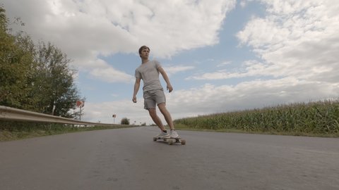 Handsome man longboarding riding skateboard cruising on countryside road on summer sunny day. วิดีโอสต็อก
