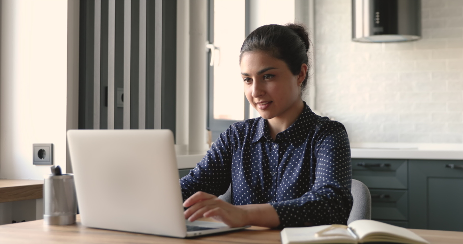 Indian 30s woman do remote job from home sit at desk smile enjoy telework activity. Spend time chatting in social networks use laptop, search helpful information for work or study on internet concept Royalty-Free Stock Footage #1058477650