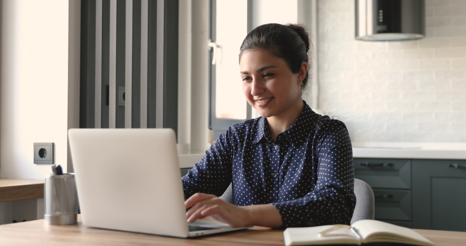 Indian 30s woman do remote job from home sit at desk smile enjoy telework activity. Spend time chatting in social networks use laptop, search helpful information for work or study on internet concept | Shutterstock HD Video #1058477650