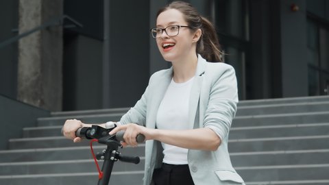 A young happy woman approaches an electric scooter and rents it with a smartphone. Scooter rental unlocking with a smartphone. Happy woman on electric scooter