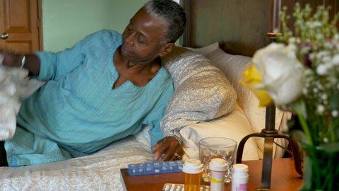 Happy elderly senior black woman with an assortment of prescription drugs on her bedside table, taking her medicine from her daily pill planner and going to sleep