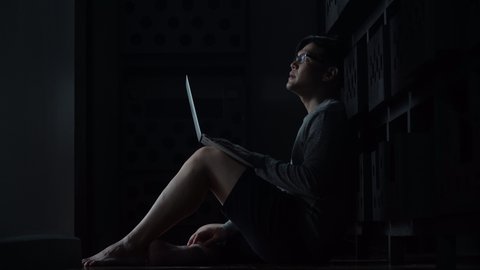 Worried young asian man sitting on the floor with laptop computerin  the dark at home 