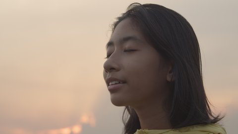 Handheld. Close up of Asian young girl happy and smile enjoying nature at sunset in the evening. side view of face teenager. Slow motion