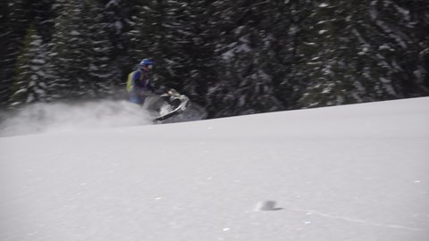 500 FPS SLO MO: Man snowmobiles up hill and makes powder turn with Grand mountains in background. snowmobilers sports riding. bright skidoo motorbike and suit. Pro snowmobiler, Winter fun moto extreme