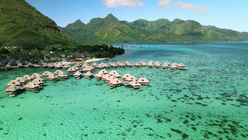 Drone aerial shot 4k. Overwater bungalows resort in coral reef lagoon ocean by beach. Paradise getaway in Moorea, French Polynesia, Tahiti. View from above glide shot. Royalty-Free Stock Footage #1058486302