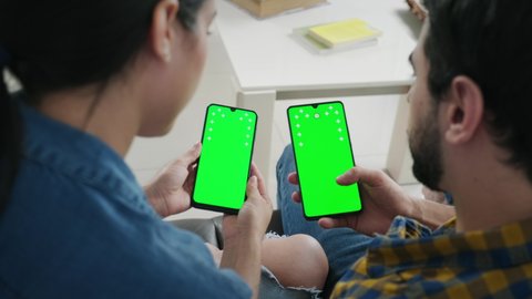 Young people using cell phones with green screen for internet and social media. Man and woman holding smartphones for web site. Boyfriend and girlfriend watching movie and photos on mobile telephones
