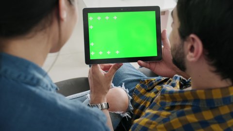 Young couple using tablet with green screen for internet and social media. Man and woman holding monitor with green monitor for website. Friends watching funny film on computer and laughing