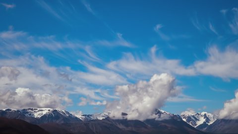 Snow covered Altai mountains peaks surrounded by fast moving clouds and fog on a summer morning. Timelapsewide angle quickly float clouds covering the snow-capped peaks of high mountains. The concept
