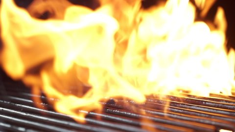 Large fresh piece of meat falls on the grill. Fire and smoke on the background. Slow motion, close-up.