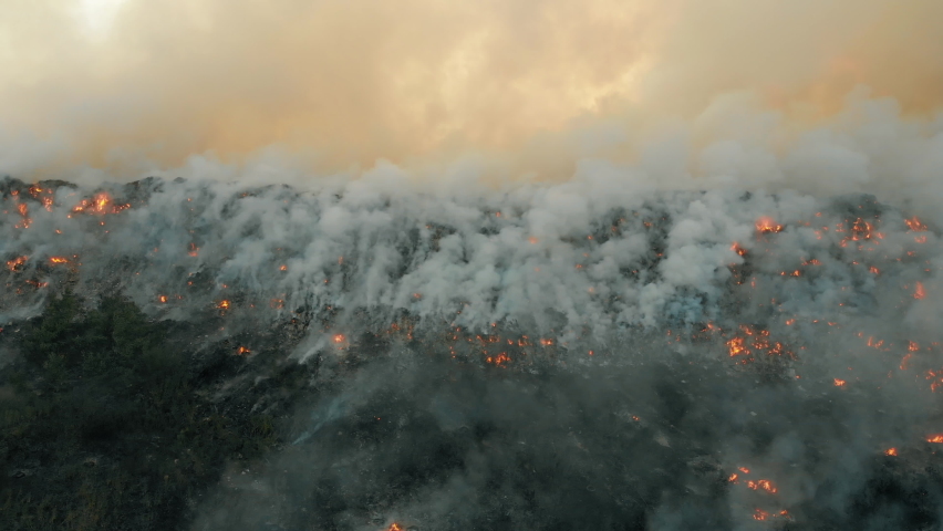 Aerial view at fire at garbage dump, burning pollutes the environment. Ecological catastrophe and destruction of nature, large fire area, camera moves into the distance Royalty-Free Stock Footage #1058496868