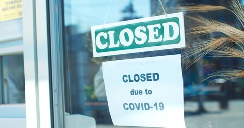 Outdoor view of window of florist store closed due to covid-19. Young female florist in apron flipping "closed" sign to "open" and ripping paper warning. Pandemic of coronavirus, healthcare.
