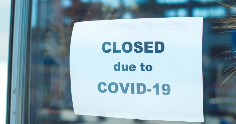Young female store owner closing shop during epidemic period. Good-looking woman florist in mask attaching paper with text "closed due to COVID-19" to window. Pandemic of coronavirus. Royalty-Free Stock Footage #1058499460