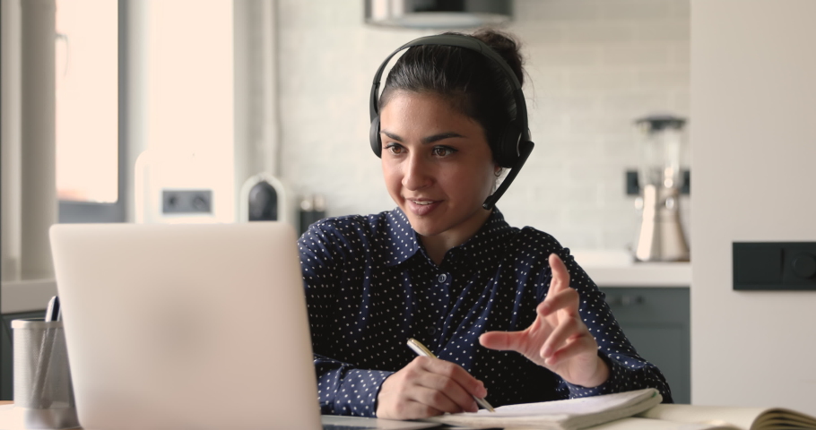 Indian student woman sit at desk at home wear headset talk distantly by video call device e-learning language. Female studying with e tutor or classmate do common task remotely. Modern tech concept Royalty-Free Stock Footage #1058499661