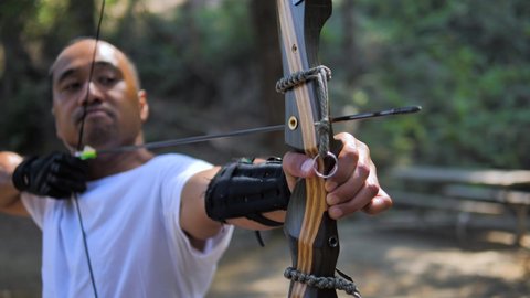 Man shoots recurve bow in slow motion in the forest. 4k footage. wire wobbles.