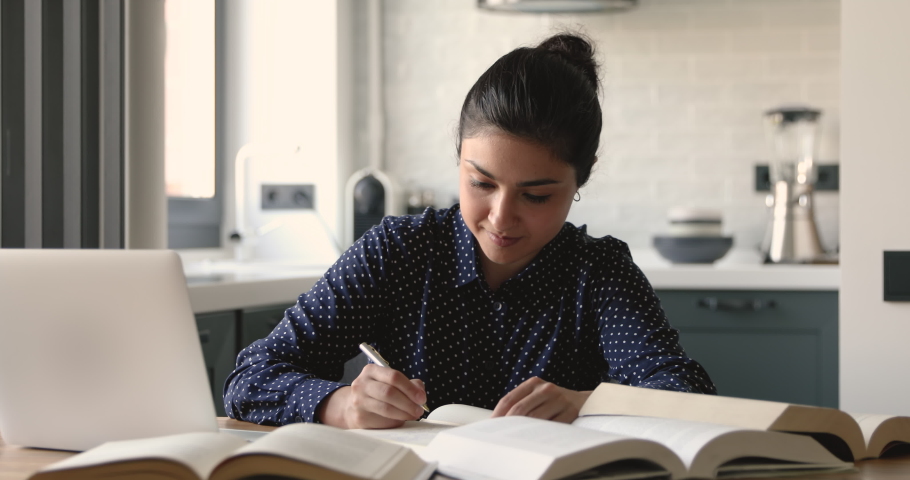 Focused attractive indian ethnicity student girl sit at desk at home noting writing down information take it from textbooks, preparing for college test or university admission, studying hard concept Royalty-Free Stock Footage #1058504095