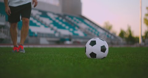 Set the socker ball on the lawn run and hit the ball in the stadium with a green lawn. A professional soccer player kicks the ball in slow motion