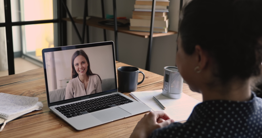 Video call event between two women best friends talk distantly, laptop screen over indian female shoulder view. People use modern tech videocall app for business or informal easy communication concept Royalty-Free Stock Footage #1058519353