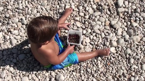 Top view on child eating sweet cherries on the beach
