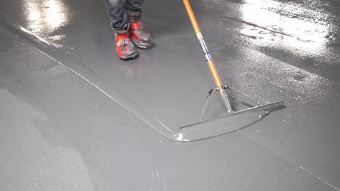 High Angle Construction Worker Applying Gray Liquid Cement Solution Coating On Concrete Floor With Squeegee,Spike Boots Floor Leveling