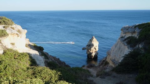 Establishing shot, Scenic view of the trail going to the rock tunnel beach in Algarve, Portugal, a boat passing by on the sea in the background.